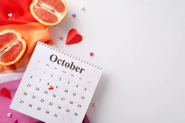 In honor of International Lesbian Day, top view image showcases lesbian flag, tiny hearts, calendar with highlighted 8th of October and two grapefruits representing female form against white backdrop