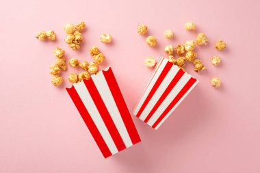 Film Sihri: Çizgili konteynırlardan fışkıran patlamış mısırın yukarıdan aşağı görüntüsü, metin veya reklamlar için pastel pembe bir zemin üzerine kurulmuş.