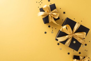 Noel Baba 'nın cazibesiyle lüks bir hediye. Üstten görünüşlü, altın arkaplanda konfeti eşliğinde parıldayan altın kurdelelerle süslenmiş siyah hediye kutuları. Tatil mesajı veya reklam ekle