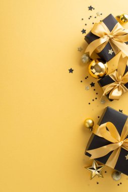 Lüks tatil cazibesi teması. Siyah hediye kutularının dikey görüntüsü, altın kurdeleler, şık ağaç ıvır zıvırları, yıldız şeklinde ışıldayan konfeti, altın fon, tatil metniniz veya pazarlamanız için yer