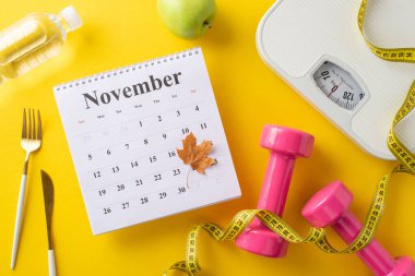 Sonbahar mevsimi vücut değişimi. Ağırlık ölçeği, mezura, pembe dambıllar, yeşil elma, su şişesi, çatal bıçak ve sarı arka planda akçaağaç yaprağı olan Kasım takvimi.