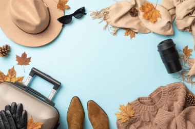 Sonbaharı sofistike bir şekilde kucaklayın. Yukarıdan bakıldığında gri bavul, kaşmir atkı, sıcak süveter, botlar ve açık mavi arka planda keçeli şapka görünüyor. Promosyon mesajınız veya mesajınız için davet alanı