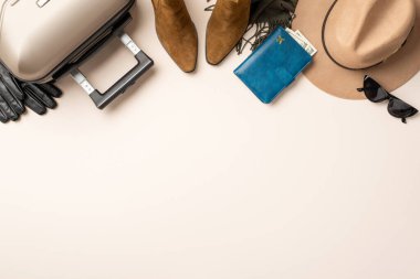 Üst görüş kompozisyonunda lüks seyahat konsepti. Keçeli şapka, kedi gözü güneş gözlüğü, eşarp, ayak bileği botları, eldivenler, bavul, içinde para olan evrak çantası yumuşak pastel yüzey biletleri, mesajınız için hazır.