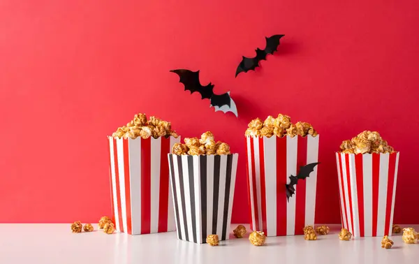 Get ready for a spooky movie night with friends! Side view of themed decor, such as flying bats and lot of popcorn boxes. Perfect for a Halloween horror movie premiere promo against a red wall
