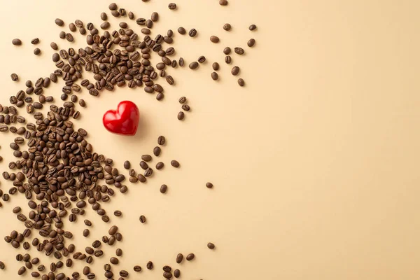 A top view perspective of a multitude of coffee beans strewn around a bold red heart, representing adoration for coffee, an excellent setting for text or advertising on pastel beige background