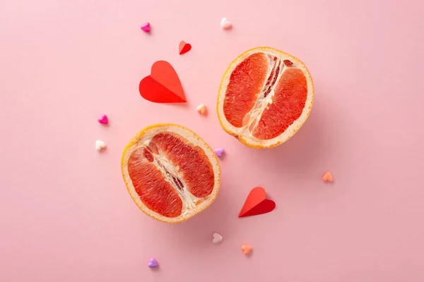 International Queer Love Day concept. Top view photo of two grapefruit halves, symbolizing feminine intimacy, and small hearts, signifying emotions, on a soft pink backdrop with room for text or ads
