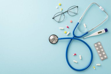 Sağlık hizmeti teması: Steteskop, gözlük, termometre, haplar, yumuşak mavi bir zemin üzerinde kabarcıklar halinde, selamlama veya tanıtımlar için geniş bir alan sunar