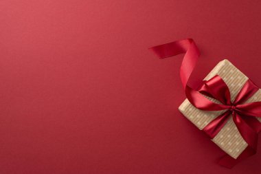 Kutlama zarafeti. Marsala arka planında kırmızı bir fiyonk ile bağlanmış el işi kağıt hediye kutusunun en üstteki görüntüsü, mesajınız veya ilanınız için odayı terk ediyor.