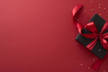 Kara Cuma şenliği sürprizi! En üstteki siyah hediye kutusu, parlak kırmızı kurdeleyle süslenmiş, altın yıldız şeklindeki konfetilerle çevrili, zengin Marsala arka planına karşı kurulmuş. Kara Cuma anlaşmaların için ideal.