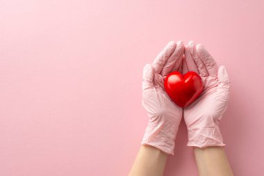 Tıp teması: Genç bir kadının ellerini ameliyat eldiveni ile sarmaladığı, kırmızı bir kalp taktığı, anneliği sembolize ettiği, mesaj ya da reklamlar için yer olan pastel pembe bir arkaplan.