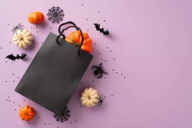 Dikkatlice seçilmiş hediyelerle Cadılar Bayramı neşesi yaratmak. Yukarıdan çekilen hediye çantası ve menekşe izole taban üzerindeki şenlikli dekorasyonlar promosyon malzemesi ya da başlıklar için telif alanı sunuyor.