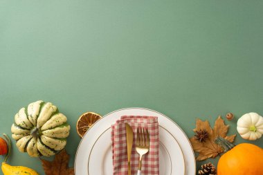 Sonbahar sezonunda Şükran Günü 'nün neşesini ailenle paylaş. İzole edilmiş yeşil zemin üzerinde yaldızlı tabakların, çatal bıçakların ve sonbahar temalı dekorun üst görüntüsü, metin veya promosyonlar için yer sunuyor