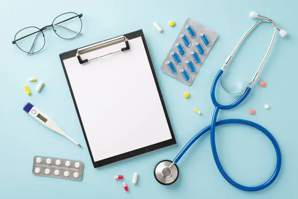 Doctor\'s Kit: Top-view shot of a stethoscope, medical clipboard, eyeglasses, thermometer, a lot of pills, against a pastel blue background. Space for your text or ad