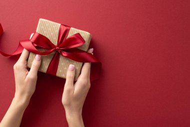 Biraz sofistike. Ellerimin üst görüntüsü Marsala yüzeyinde kırmızı kurdeleyle süslenmiş şık bir hediye kutusuyla etkileşime giriyor. Metnin ya da ilanın için yer var.