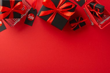Tasarruf Mevsimi Keyfi: Kırmızı kurdele fiyonklarının yer aldığı siyah hediye kutularının üst görünümü, kırmızı zemin üzerinde 