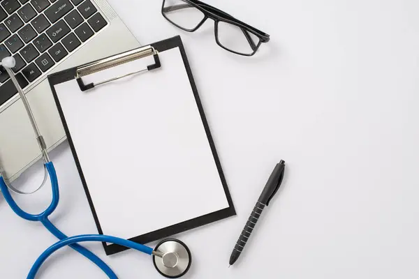 Online healthcare visit concept. Top view of laptop, stethoscope, medical survey clipboard, eyeglasses, and pen set up on white background with room for text or advertising