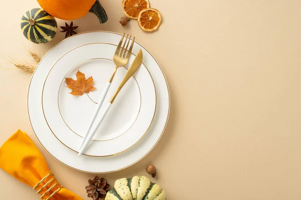 Autumnal scene of Thanksgiving family dinner is portrayed from above. Gilded plates, vintage cutlery, and fall-themed ornaments rest on beige isolated background, perfect for text or adverts