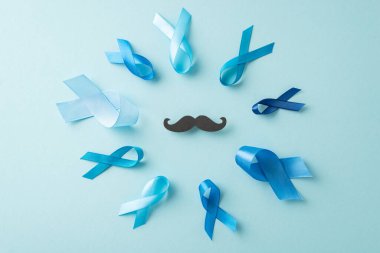 Prostat kanserine karşı savaşan erkeklerin birlikteliğini sembolize ediyor: Mavi kurdelelerin üst görüntüsü, ortada bıyık siluetiyle çember oluşturuyor - reklamlar için yumuşak mavi yüzey üzerindeki erkeklerin gücünü simgeliyor