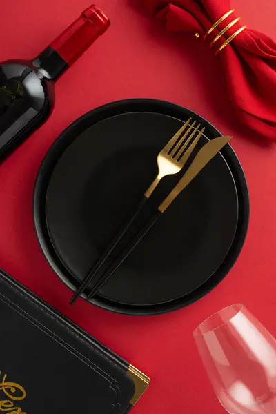 Exclusive Black Friday Dining: Overhead vertical view of table adorned with black plates, gold cutlery, red napkin, menu, wine, and glass on sleek red surface for your advertising