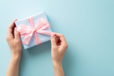 Birinci şahıstan size: Pastel mavisi hediye kutusundaki kurdeleyi çözen kadın elleri, puantiyelerle süslenmiş, Pastel mavisi arka planda, mesajınız ya da reklamınız için hazır.