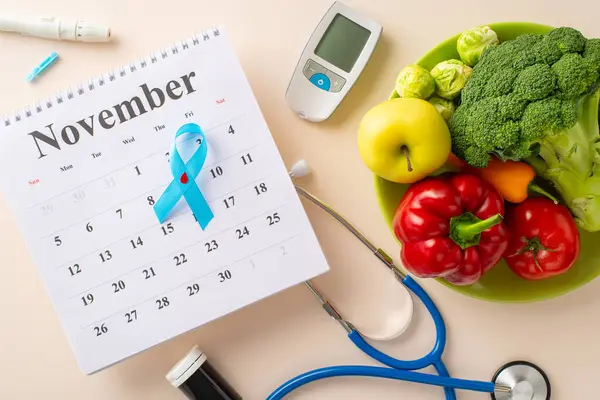 Scheduled diabetes check-up during Diabetes Awareness Month. Top view of calendar adorned with diabetes emblem, glucometer kit, stethoscope, plate with vegetables and fruits on a pastel beige backdrop