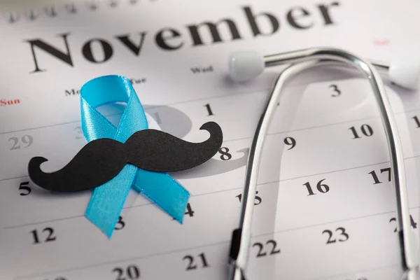 November\'s Men\'s Health Promotion. Closeup of prostate cancer awareness emblem - blue ribbon, mustache, stethoscope on calendar background. Encouraging check-ups