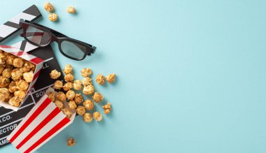Film şeridinin ilk gösterimini bekliyorum. Yapımcının en iyi görüntüsü, 3 boyutlu göz giysisi, çizgili kutulardan yayılmış nefis patlamış mısır, açık mavi arka planda mesaj veya promosyon için boş alan.