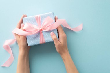 Kutlama hediyesi: ellerimin üst görünüşü pastel mavi bir hediye kutusunu, benekli desenini ve pembe kurdele şeklindeki zevkini beşikte tutuyor. Pastel mavisi bir ortam sözlerinizi hoş karşılar.