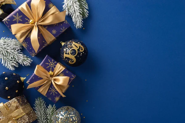 Shimmering Holiday Gift Suggestions. Overhead shot of glistening gold and blue wrapped gifts, ornaments, shimmering confetti, and frosted branches on a blue backdrop, perfect for festive greetings