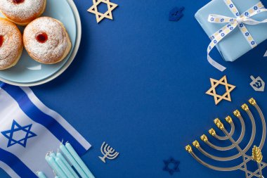 Engage in Hanukkah customs with a top-view shot showcasing sufganiyot, Star of David symbols, Israeli flag, gift box with ribbon bow, menorah on blue backdrop, offering space for text or promo content clipart