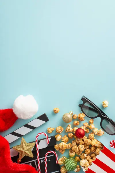 Christmas filmstrip designed around popcorn concept. Top-view vertical shot of producer\'s movie clapper, popcorn, gleaming baubles and more on light blue backdrop. Open area for text or film promo