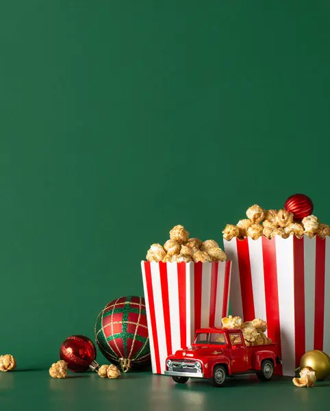 Opt for stay-at-home holiday experience with delivery idea. This side vertical view image captures tabletop featuring popcorn, festive baubles, tiny car on green wall backdrop, ideal for movie advert or promo
