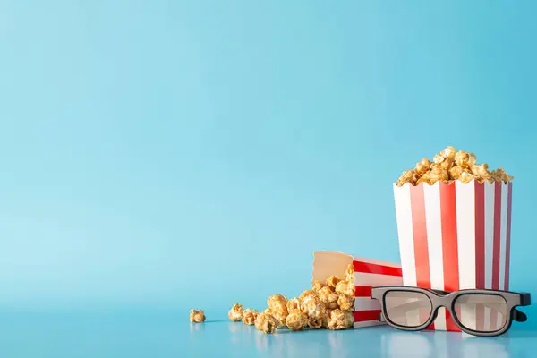 Film fest with buddies and munchies theme. Side view photograph of a tabletop with scrumptious popcorn in striped containers and 3D glasses on pastel blue backdrop, ideal for movie promo