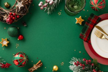 Şenlikli yemek düzeneği tasarımı. Genel bakış tabakları, çatal bıçak takımı, kareli peçete, şarap kadehi, takılar, doğal çelenk, konfeti, buzlu köknar, yeşil arka planda ökseotu, yazı için boş alan