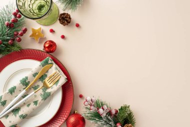 Şenlikli yeni yıl yemeği için lüks masa düzenlemesi. Üst tabaklar, altın çatal bıçak, peçete, şarap bardağı, tatil takıları, mum ışığı, köknar dalları, yazı veya reklam için bej arka planda ökse otu.