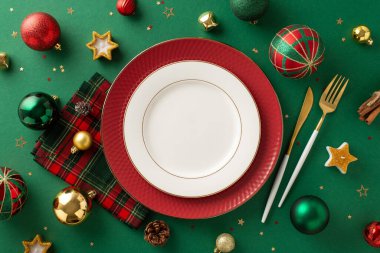 Elegant holiday dinner table setting. Overhead perspective of plates, golden cutlery, plaid napkin, baubles, pine cone, cinnamon sticks, star candles, sparkling confetti on a green background clipart