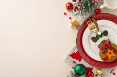 Tatil temalı çocuk masası: Üst görünüm tabakları, yaldızlı çatal bıçaklar, peçete, kupa, takılar, yıldız mumu, buzlu çam dalları, pastel bej arka planda ökseotu çilekleri