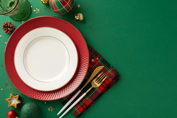 stock image Stylish dinner table decor concept. Top view of plates, golden utensils, checkered napkin, wine glass, ornaments, pine cone, star-shaped candle, shimmering confetti on green surface for text or advert