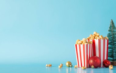 Kış filmlerine alışın çizgili patlamış mısır kutuları, süsler ve film promosyonları için pastel mavi bir duvara yaslanmış küçük bir Noel ağacı.
