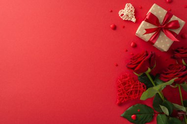 Sevgililer Günü romantizm fikri. El işi kâğıdı hediye paketi, rattan kalp dekoru, kırmızı gül buketi, mesajınız için kırmızı yüzeyde şeker parçacıkları.