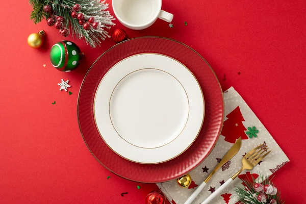 Chic New Year\'s dinner table arrangement for a family gathering from top view. Gold cutlery, cup, baubles, plates, and festive adornments on a red background, with space for text or advertisements