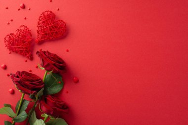 Sevgi dolu Sevgililer Günü tasarımı. Üzerinde rattan kalp süslemeleri, kırmızı bir gül buketi ve kırmızı bir yüzey üzerinde sürüklenen şeker tanecikleri olan yazı veya promosyonlar için yeri olan üstten çekim