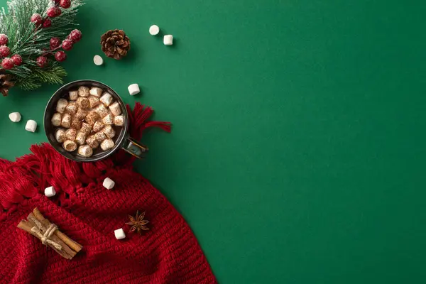 Find warmth in winter with a top-view capture of a delightful hot chocolate, marshmallow, spices, red knitted scarf and festive decorations on deep green backdrop