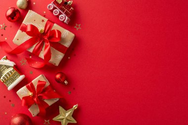 Yeni yıl için şenlik hazırlığı. Zanaatın üst görüntüsü, kırmızı ve altın takılarla süslenmiş, tren ve ev gibi tuhaf Noel ağacı heykelcikleri, konfeti, metin için yeri olan canlı kırmızı yüzey