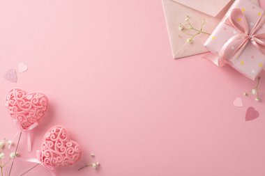 Sevgililer Günü 'nde sevgiyi bu yukarıdaki manzarayla paylaş. Hediye kutusu, çingene, kalp şeklinde konfeti, davetiye zarfı, çubuklardaki kalp dekoru pastel pembe bir yüzey üzerinde romantik bir sahne oluşturur.