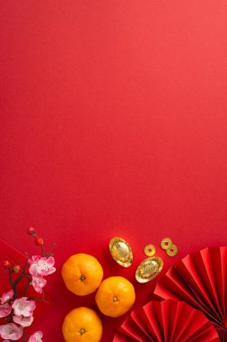 Büyüleyici Ay Yeni Yılı kompozisyonu. Dikey üst görünüm hayranları, feng shui öğeleri, madeni paralar, sycee, Hong Bao, mandalina, kırmızı arkaplanda sakura, metin veya tanıtım içeriği için boş bir alan
