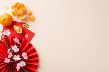 Yeni yıl kutlamalarını bu büyüleyici beste ile başlatın. Kırmızı fanın yukarıdan aşağı görüntüsü, feng shui süslemeleri, şanslı paralar, kırmızı zarflar, nötr arkaplanda soyulmuş mandalinalar, metin için boşluk