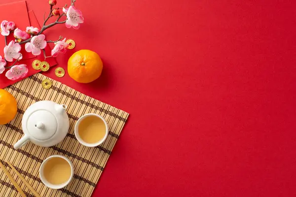 Chinese New Year Feast Arrangement: top view tea ceremony set, chopsticks, bamboo placemat, traditional coins, Hong Bao, tangerine fruits, sakura on red backdrop. Advertise in this festive setting
