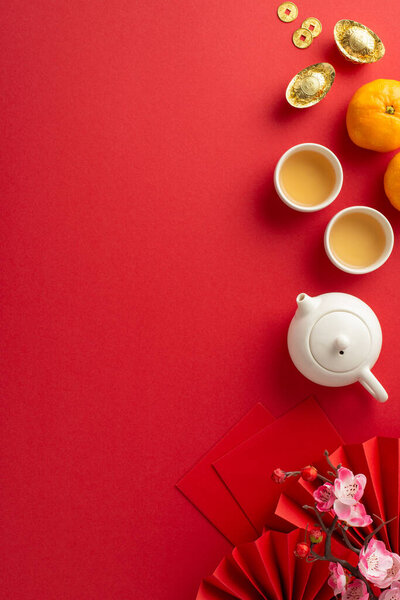 Dive into richness of Chinese New Year with sumptuous table setting. Overhead vertical shot of ornate fans, green tea accessories, Feng Shui symbols, citrus, sakura on red canvas, ready for your ad