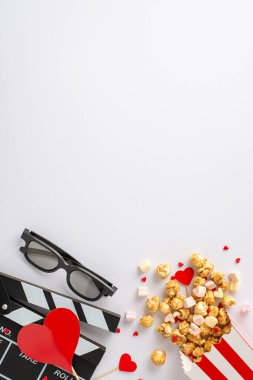 Sevgililer Günü 'nde aşk dolu bir film izlemek. Dikey alkış tahtası, 3D gözlükler, çizgili patlamış mısır kutusu, kalp dekor, lokum ve şekerleme. Metin veya reklamlar için boşluk olan beyaz arkaplan